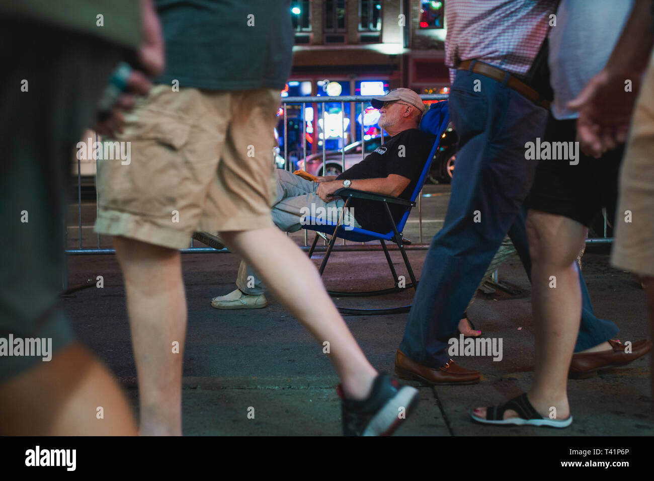 Un uomo in una sedia a dondolo siede sul marciapiede affollato al di fuori di una discoteca Foto Stock