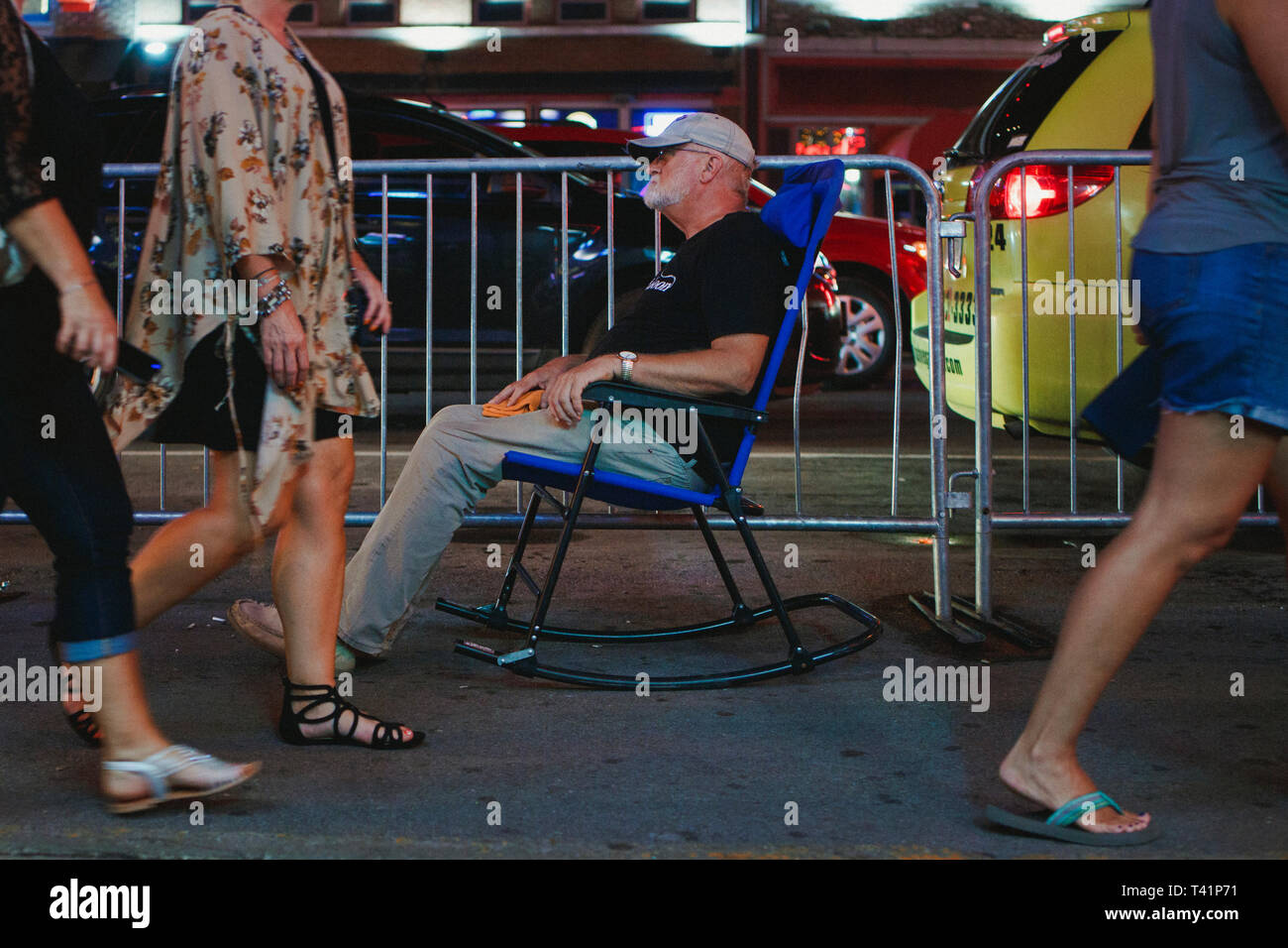 Un uomo si siede in un bilanciere nel mezzo di un affollato marciapiede di notte Foto Stock