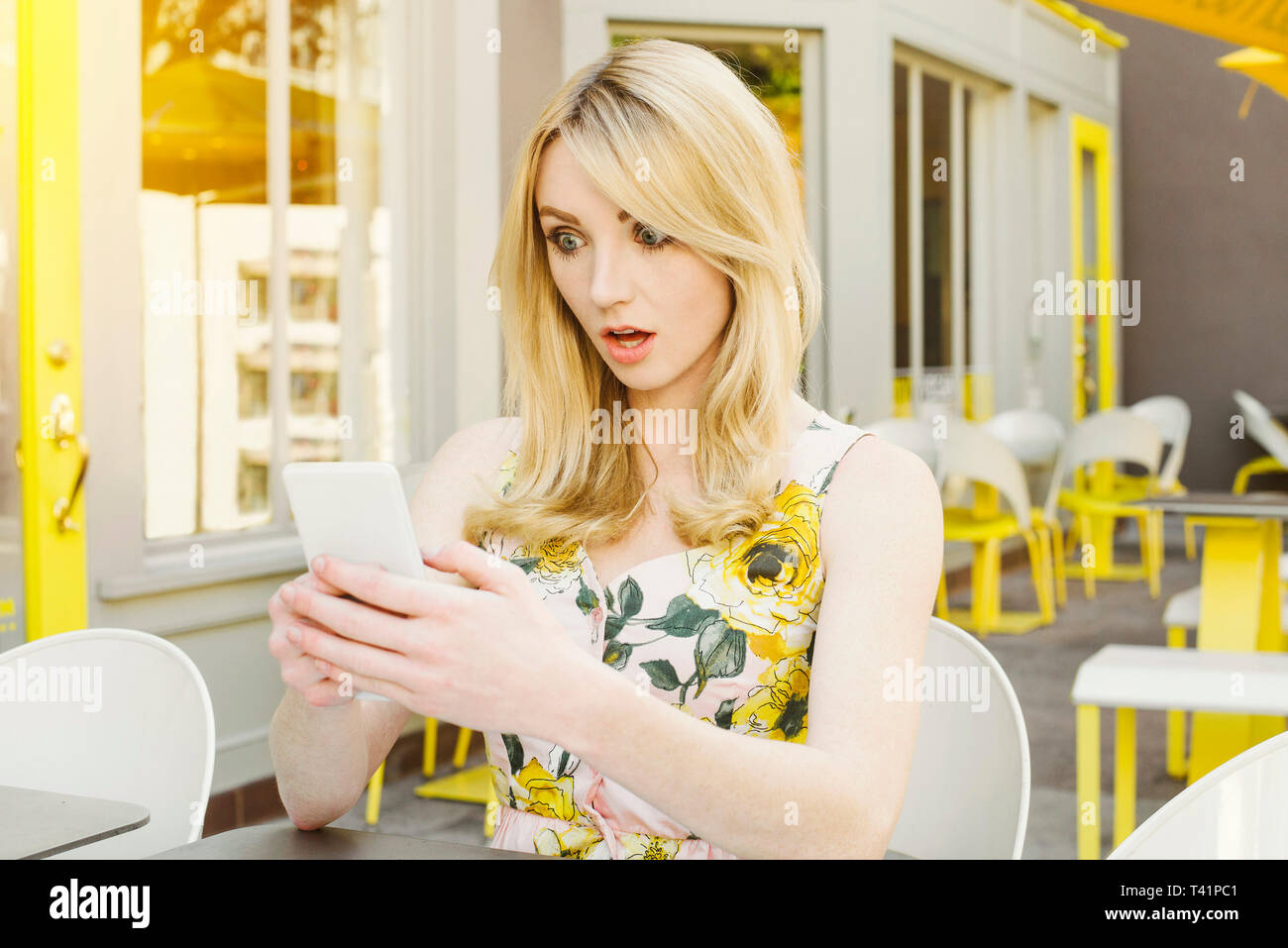 Pretty Woman è scandalizzato per foto o testo che è sul suo smart phone a un cafe' all'aperto Foto Stock