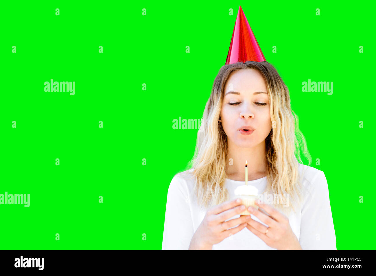 Una millenaria donna con capelli biondi celebra un compleanno con una festa di compleanno cupcake e compleanno hat. Brucia la candela Foto Stock