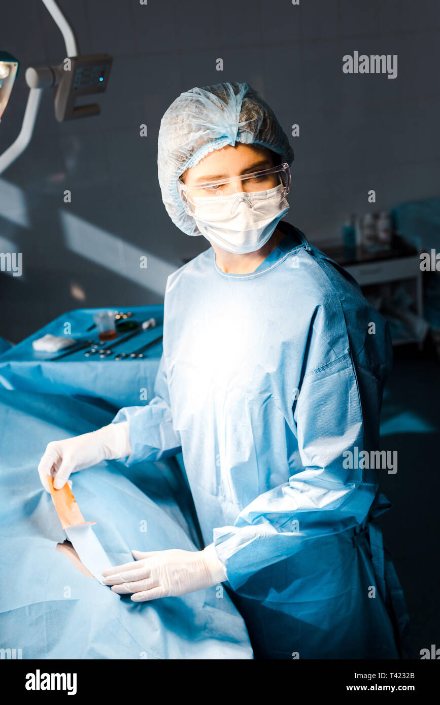 Infermiera in uniforme e cappuccio medica mettendo sul nastro in sala operatoria Foto Stock