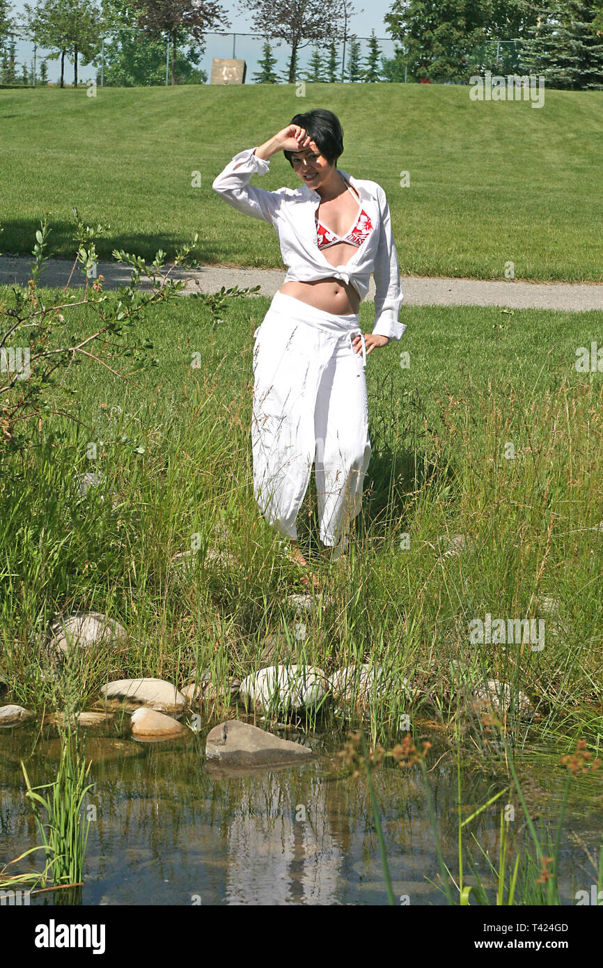 Dai capelli scuri bella donna in posa di un parco che indossa un rosso e bianco top bikini, bianco giacca e pantalone Foto Stock