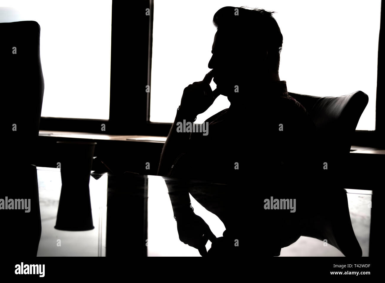 Silhouette nera dell'uomo a tavola, pensando malinconici pensieri profondi. Foto Stock