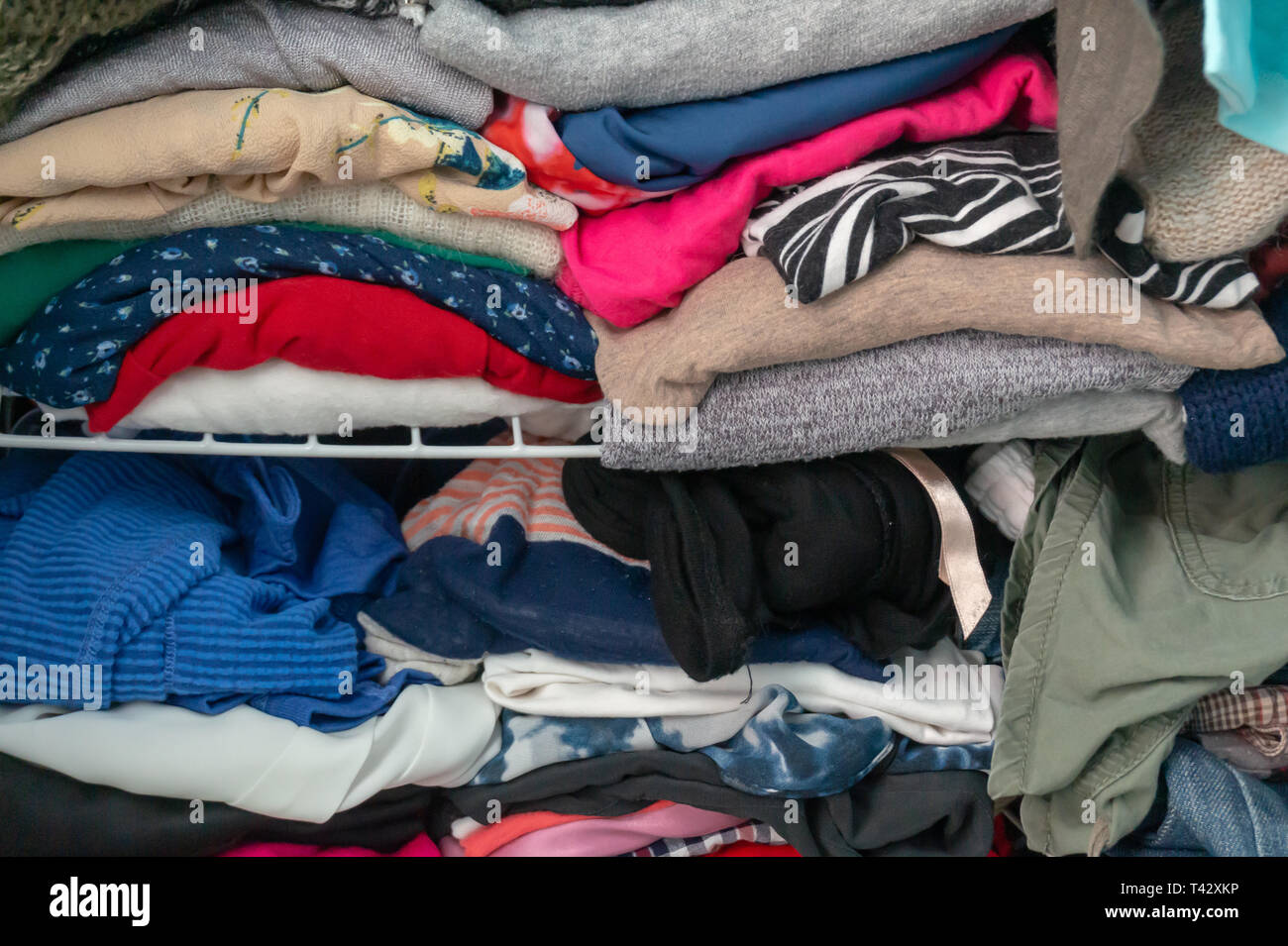 Confuso piegato vestiti stipati in un armadio su un ripiano. Raffigurante una donna guardaroba, consumismo, pulizia e riassetto giornaliero, spurgo, ecc. Foto Stock