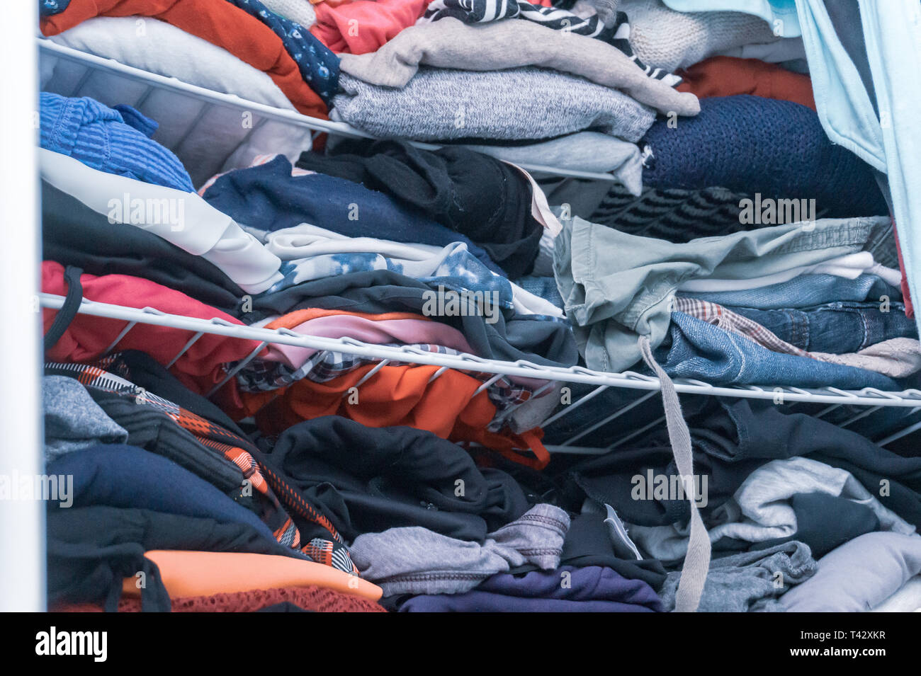 Blu e rosso di tonalità di abbigliamento in una donna di armadio, piegato ma confuso, in necessità di organizzazione di armadio. Raffigurante la donazione di vestiti, riordino. Foto Stock