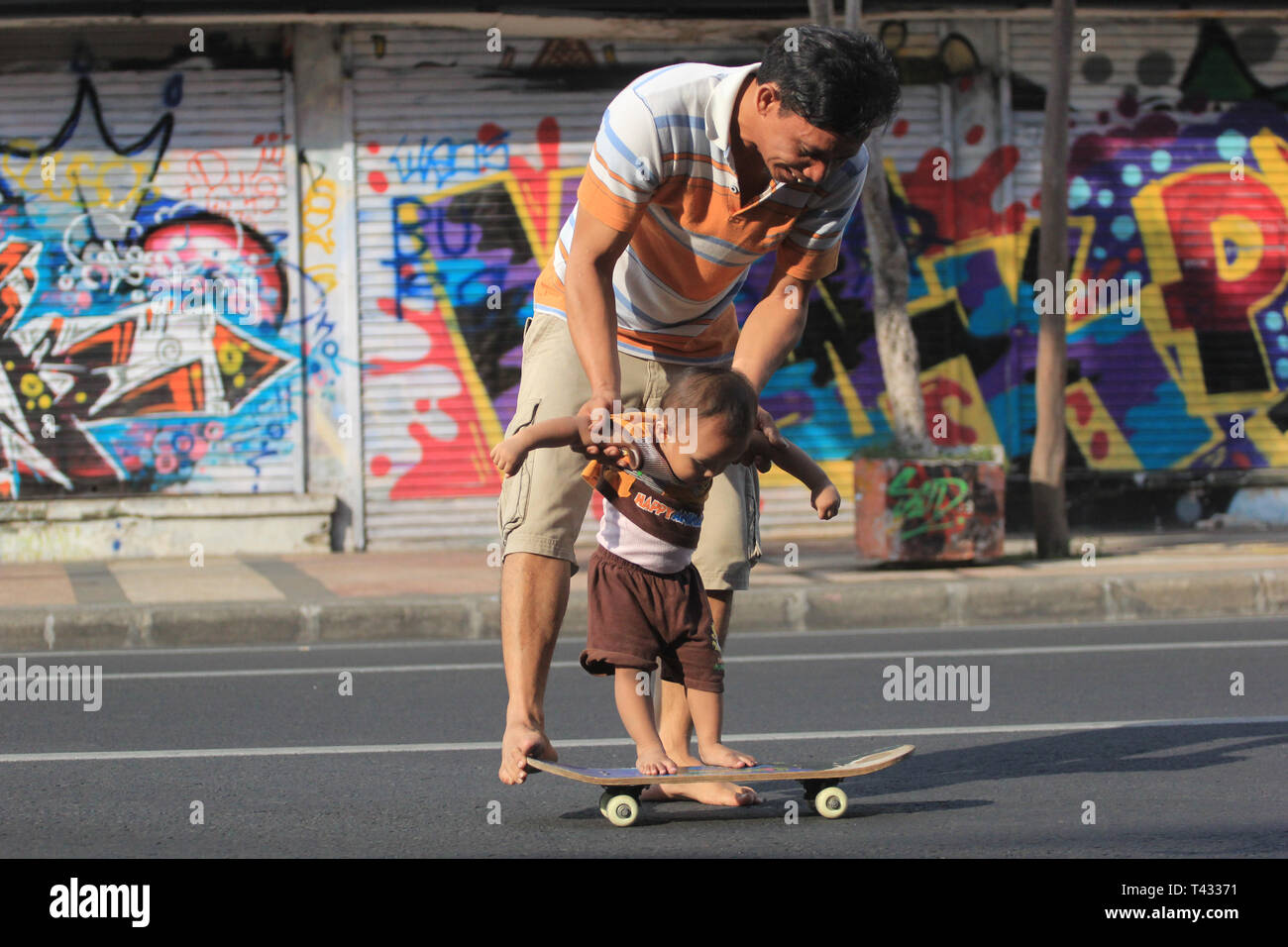 Surabaya Indonesia, 13 dicembre 2015. Un padre gioca skateboard con il suo bambino Foto Stock