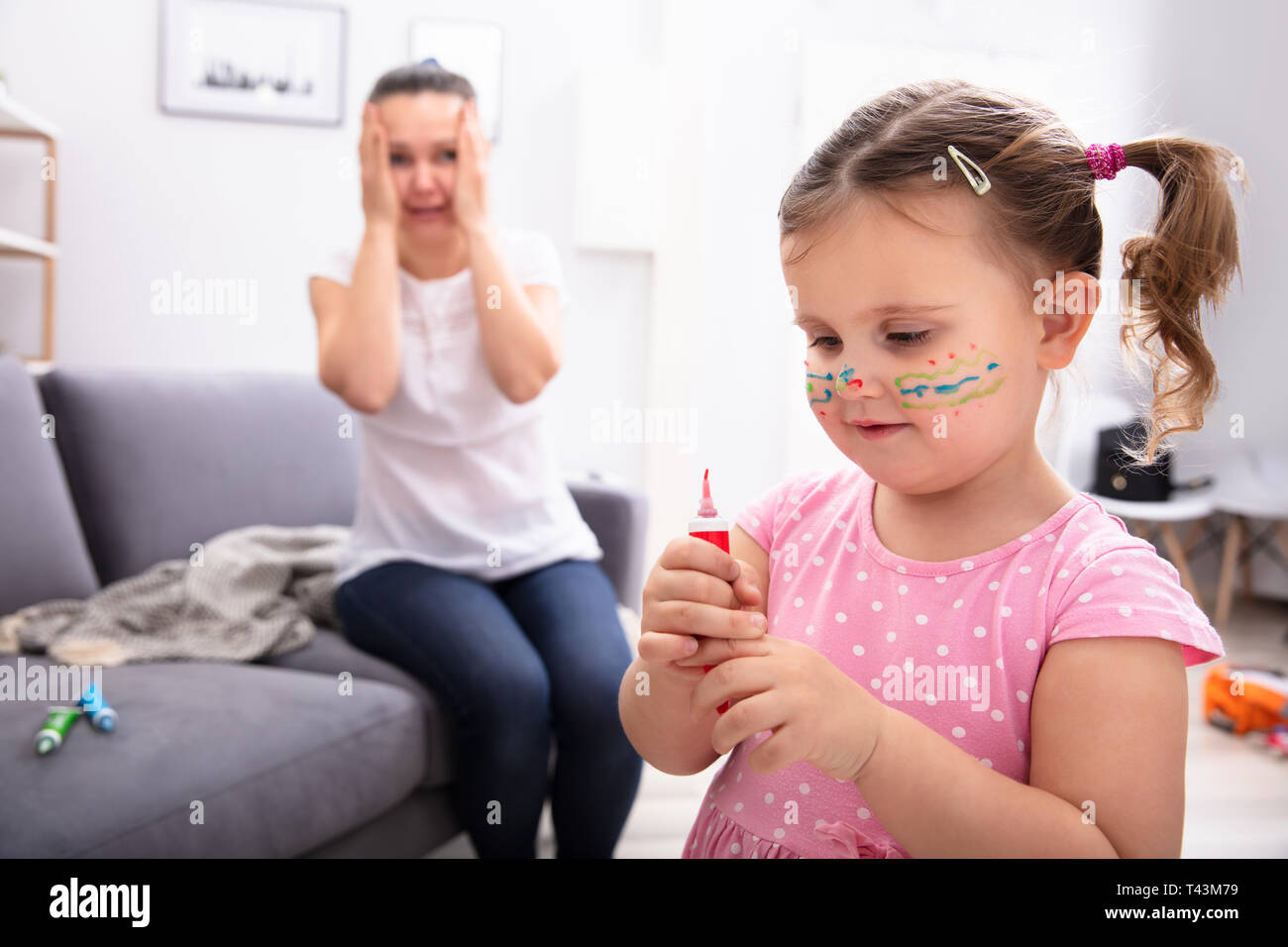 Scioccato la madre seduta sul divano guardando la figlia volto dipinto con tubo a colori Foto Stock