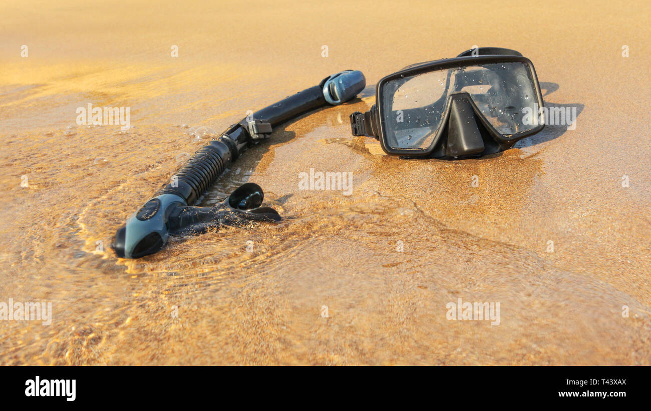Sole che splende al nero di snorkelling e immersioni subacquee maschera sulla spiaggia bagnata sabbia lavata dal mare. Foto Stock