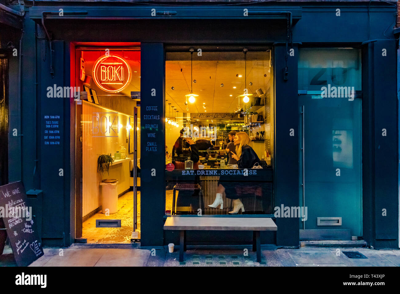 Una donna si siede ad un tavolo vicino alla finestra illuminata di Boki, un caffè indipendente a Seven Dials, Londra, Regno Unito Foto Stock