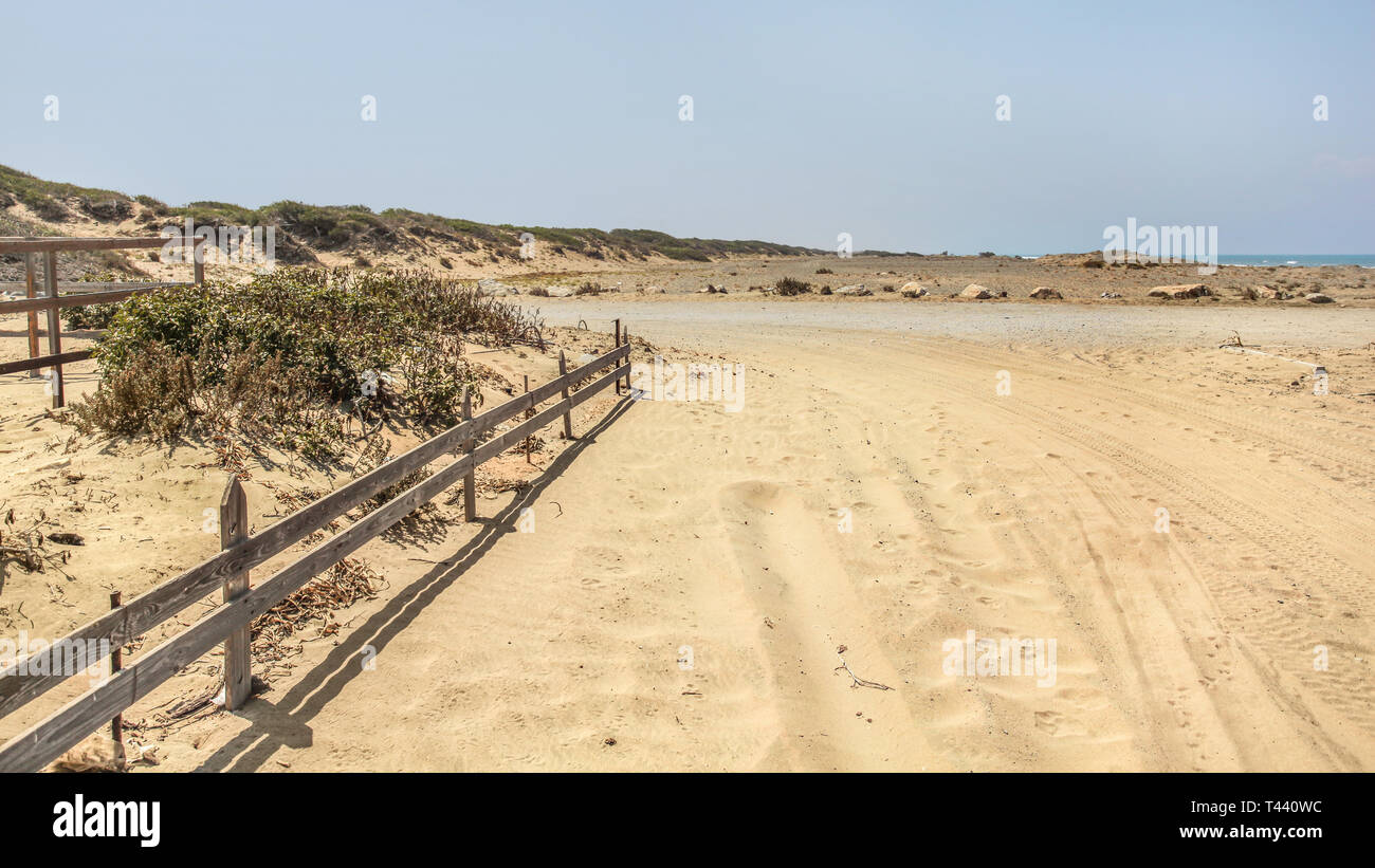 Pneumatico e piedi stampe su una strada che conduce alla spiaggia coperta di sabbia. Mare distante in background. Foto Stock