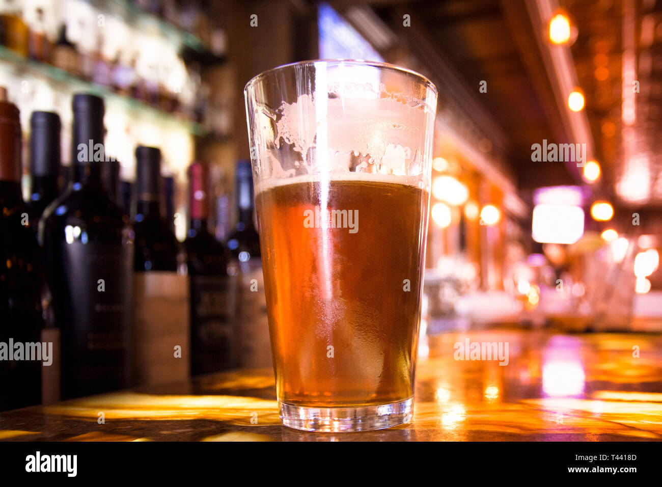 Bicchiere di pinta di birra ambrata con colorati di sfocatura di bar in background Foto Stock