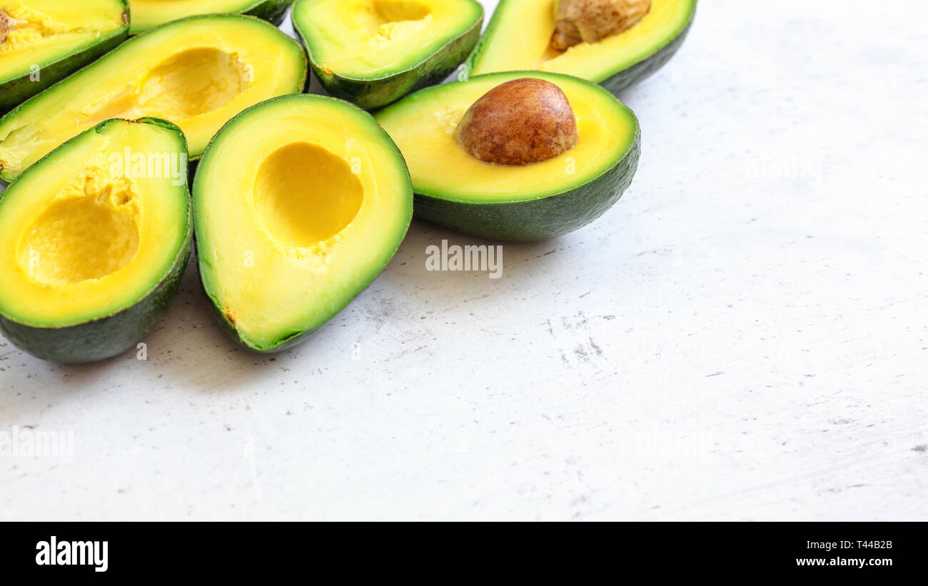 Dimezzato avocado verde con polpa di colore giallo, alcuni semi marrone visibile sul bianco della scheda di lavoro - lo spazio per il testo a destra Foto Stock