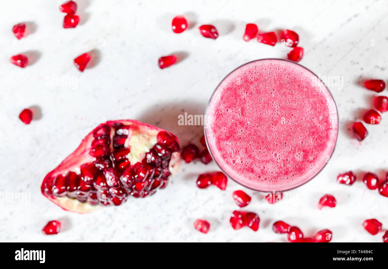 Frullato di melograno con gemma sfocata come frutti sparsi nei pressi di sul pannello bianco. Foto da sopra, concentrarsi sulle bolle nella schiuma di bere Foto Stock