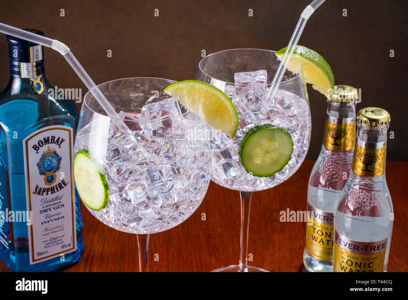 Gin Tonic, stile moderno - globo di vetro, lotti di ghiaccio, fette di cetriolo e calce e una paglia Foto Stock