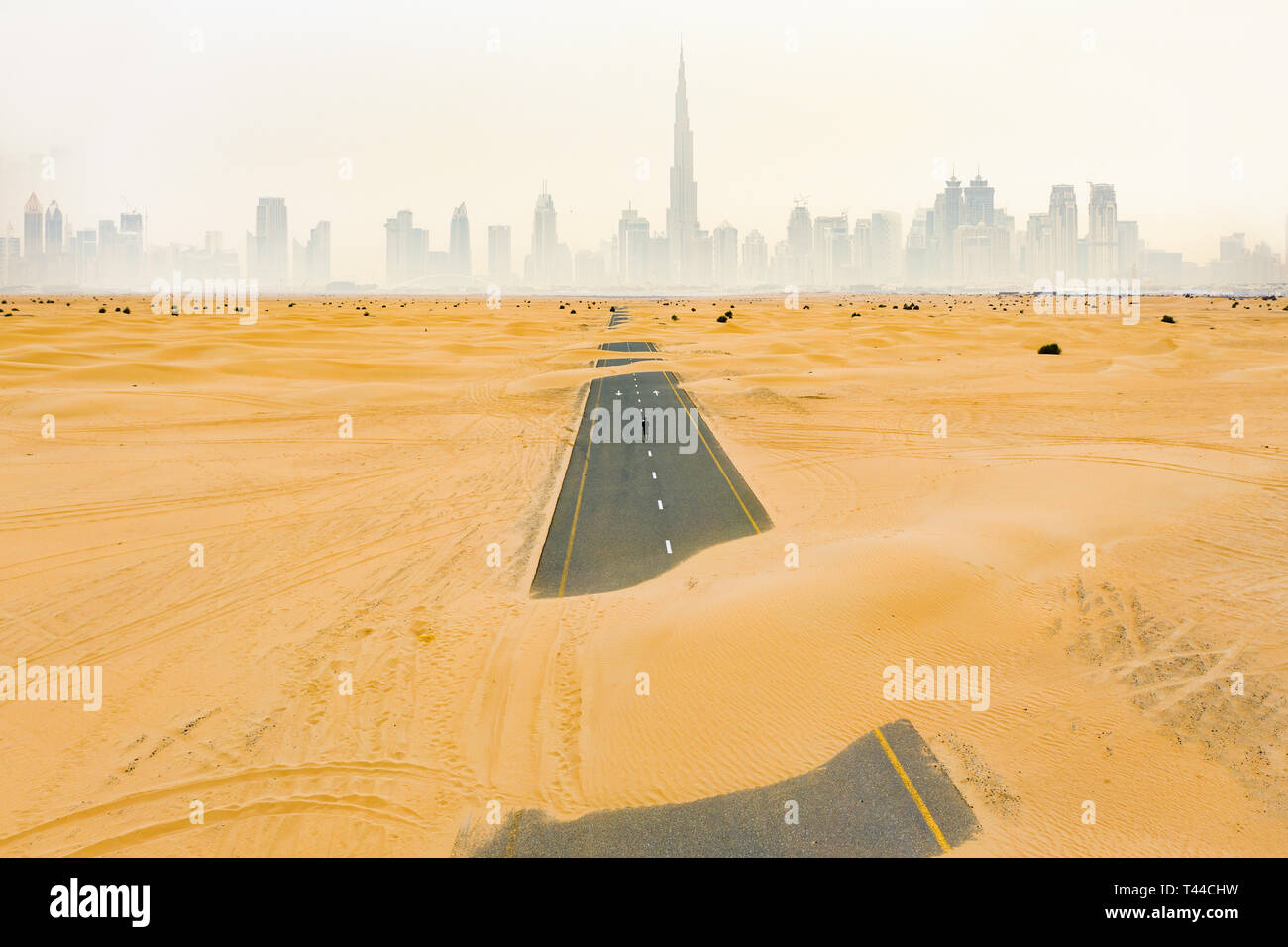 Incredibile vista aerea di una persona non identificata a camminare su una strada deserta coperta da dune di sabbia nel deserto di Dubai. Skyline di Dubai circondato da nebbia Foto Stock