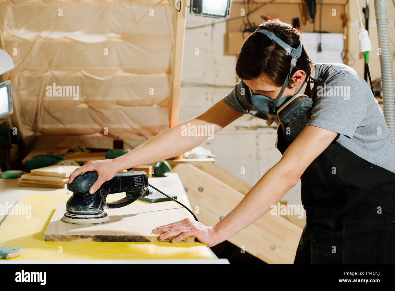 Ritratto di lavoro slim bello di mezza età brunet carpenter nel respiratore. Egli sta rendendo mobili su ordine in un workshop. Levigatura del pannello di legno surf Foto Stock