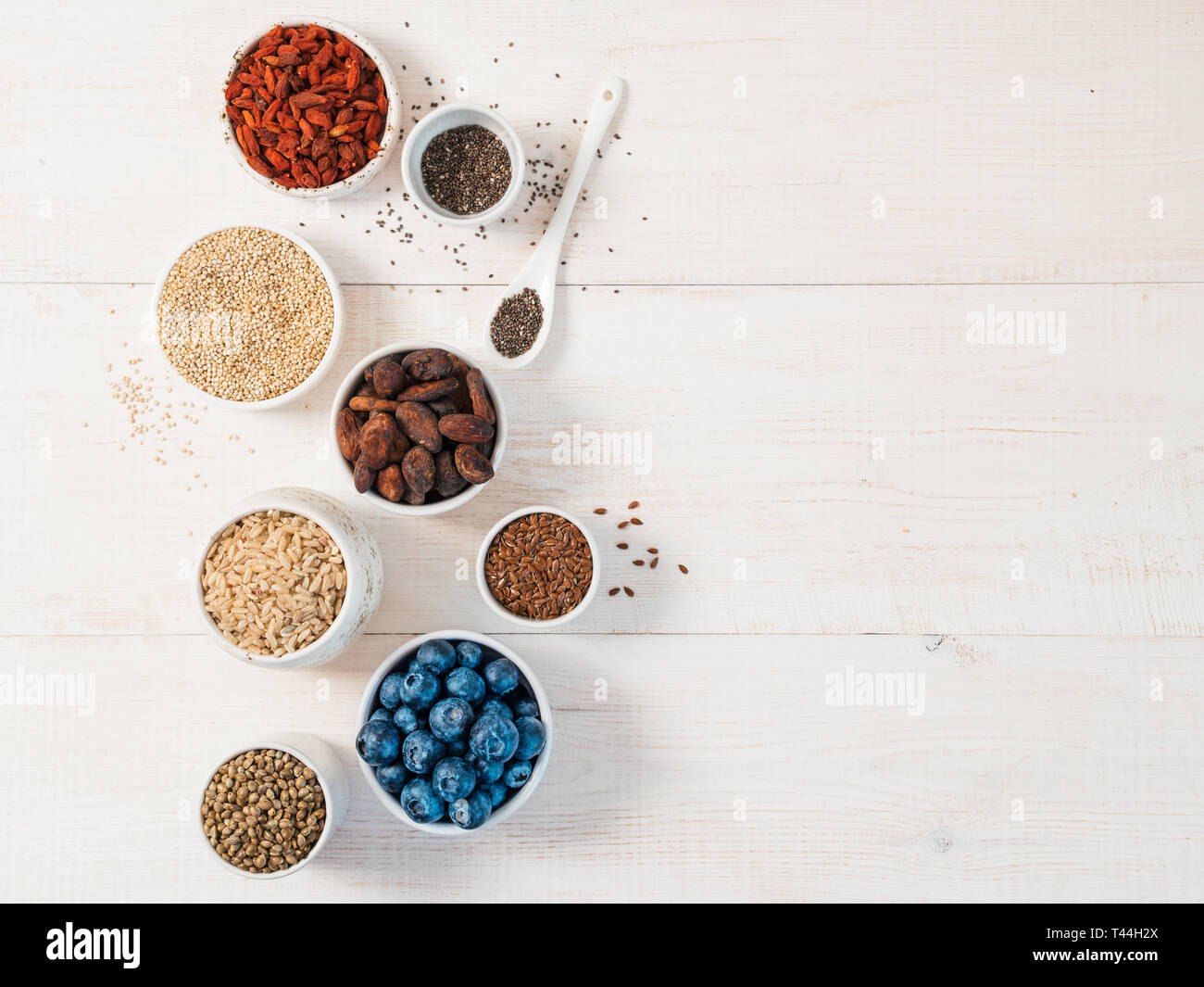 Varie superfoods in una piccola ciotola su bianco tavolo in legno.Selezione super food.Super come mirtillo, chia, materie fava di cacao, goji, sementi di canapa, quinoa, riso marrone. Copia spazio per il testo.vista superiore o laici piatta Foto Stock