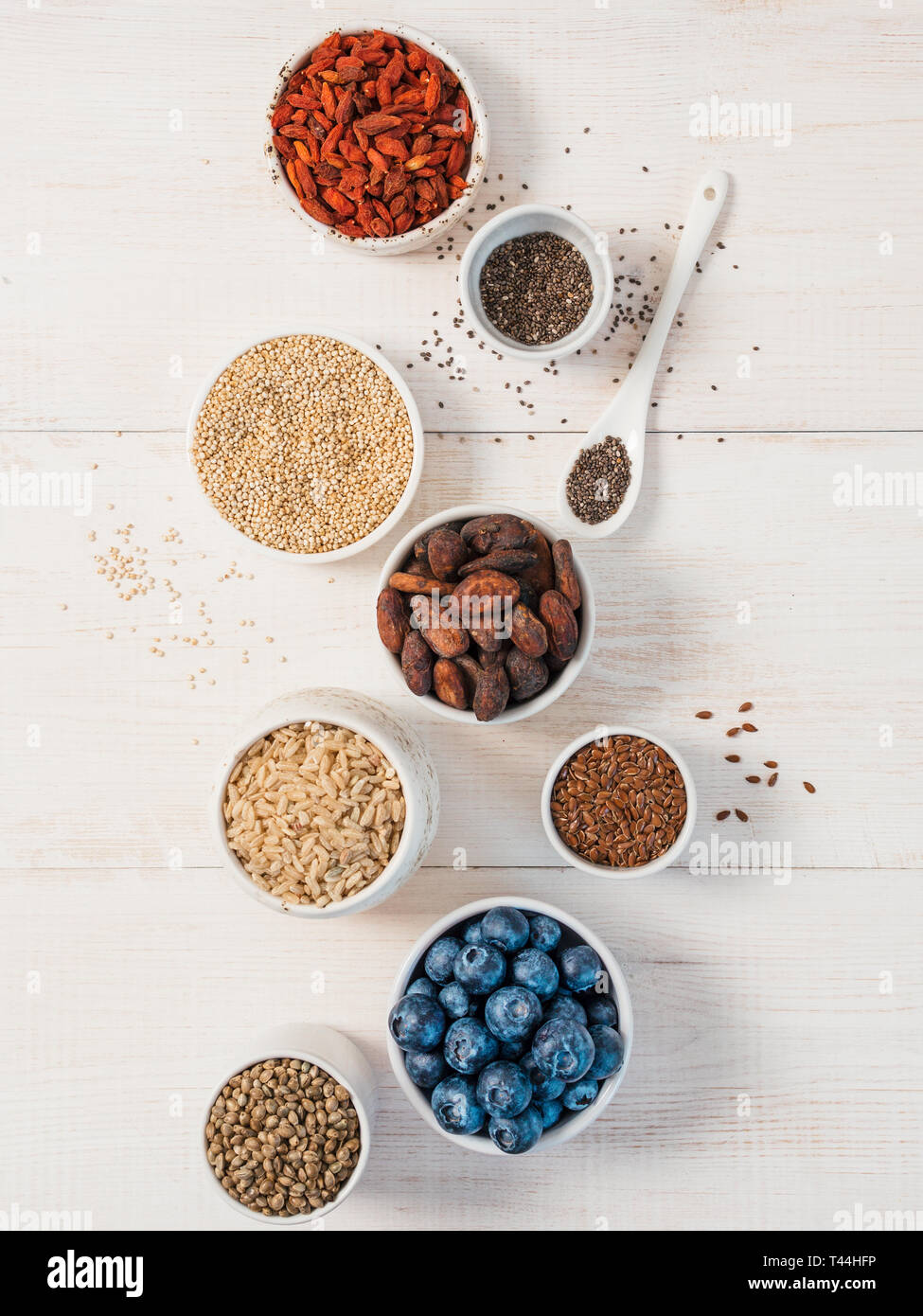 Varie superfoods in una piccola ciotola su bianco tavolo in legno.Selezione super food.Super come mirtillo, chia, materie fava di cacao, goji, sementi di canapa, quinoa, riso marrone. Spazio di copia.vista superiore o piatta lay.verticale Foto Stock