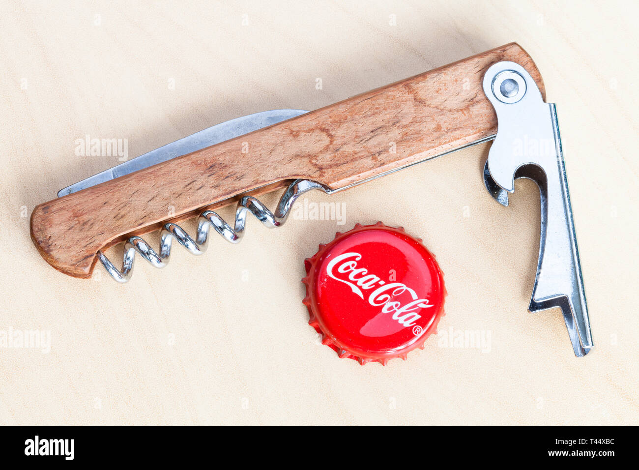 Mosca, Russia - aprile 4, 2019: usato crown cork tappo di bottiglia da bevande Coca-Cola e apribottiglie sulla tavola di legno. La coca cola (coke) è gassata s Foto Stock
