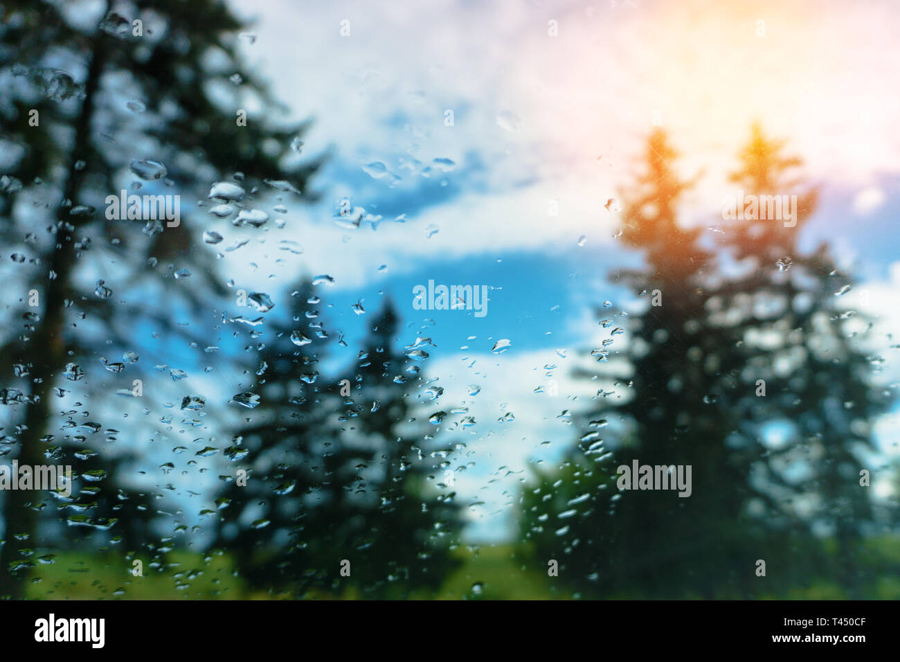 Sul vetro della goccia di pioggia. al di fuori della finestra il sole di nuvole e il blu del cielo. contro lo sfondo di alberi Foto Stock
