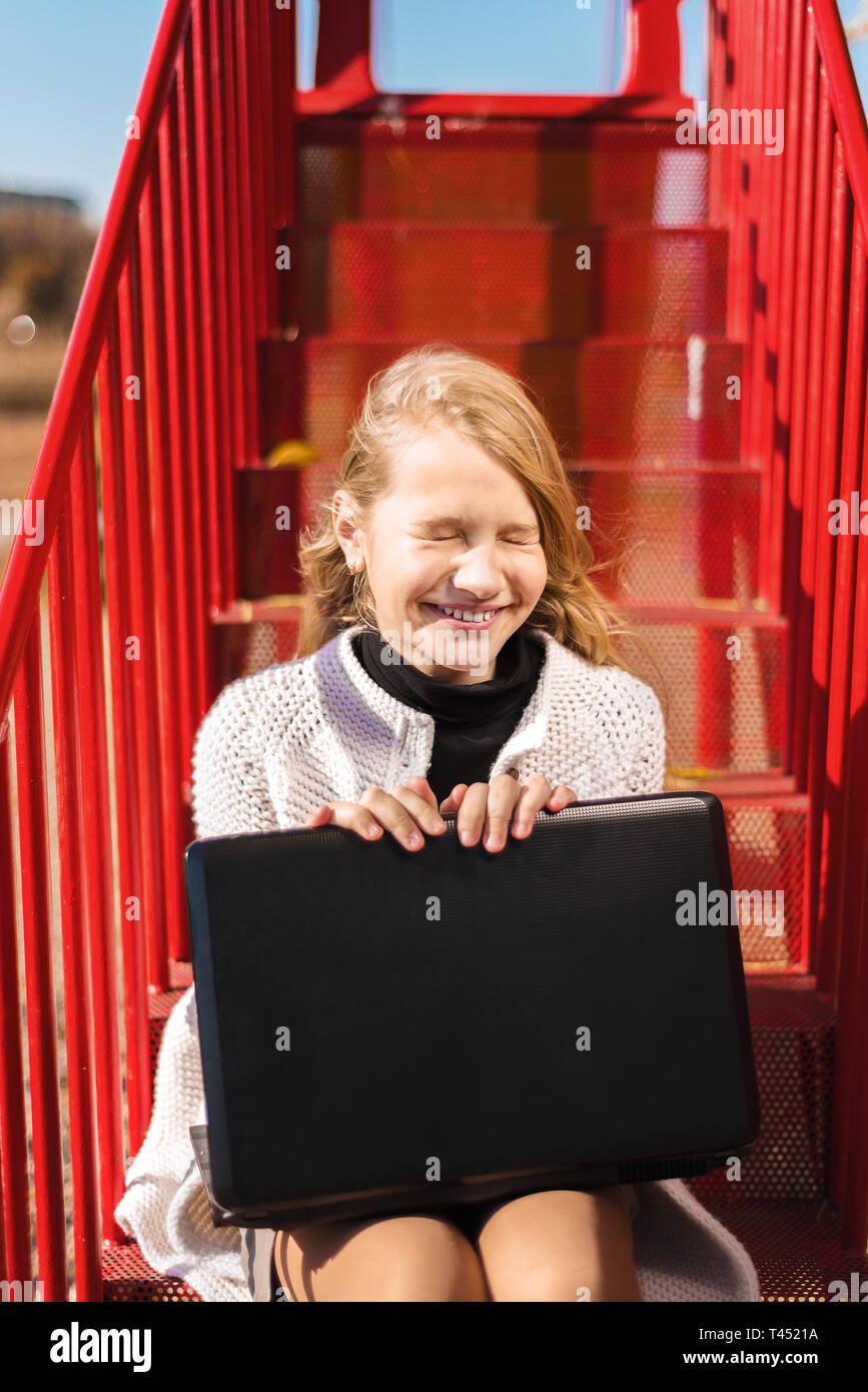 Felice studente sorrisi. ragazza ride. adolescente seduta sulle scale di colore rosso e la holding laptop Foto Stock