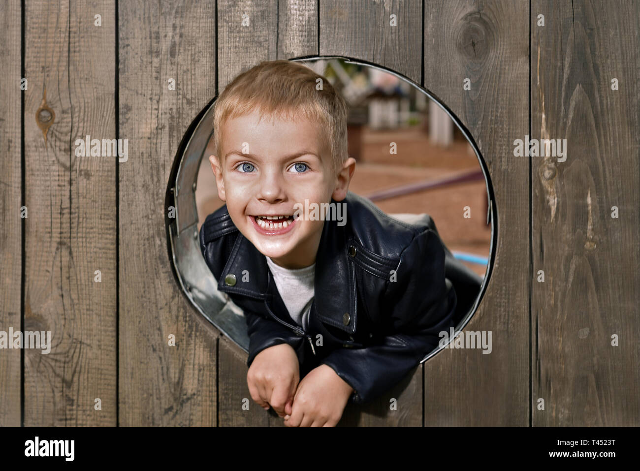 Ritratto di felice little boy. Il bambino guarda fuori del turno di finestra in legno e sorridente Foto Stock