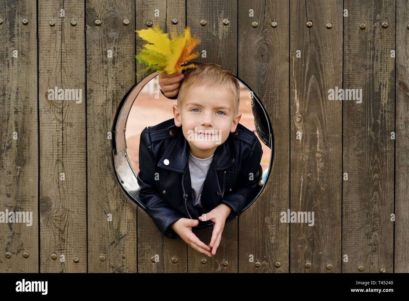 Ritratto di felice little boy il capretto sta guardando fuori del turno di finestra in legno e sorridente Foto Stock