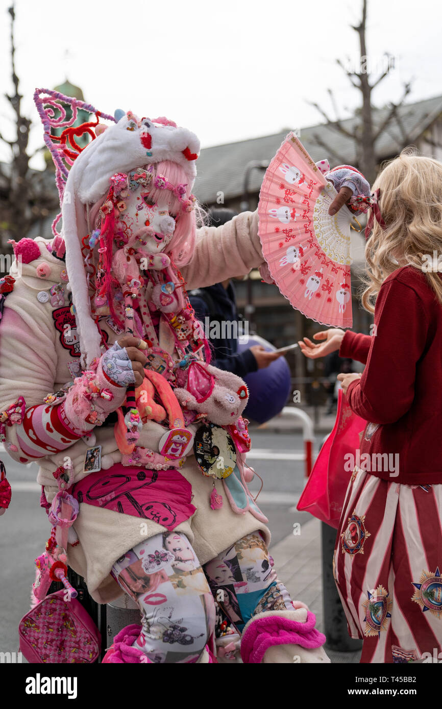 Tokyo, Harajuku è il gioco cos il centro di Tokyo con vari giovani mode in evidenza. Questo uomo, noto come Kadocchi, è considerato come egli unoffical icona di Harajuku. Uomo vestito da clown in rosa e bianco vestito mantenendo la ventola, in posa per il visualizzatore. Contatto visivo. Foto Stock