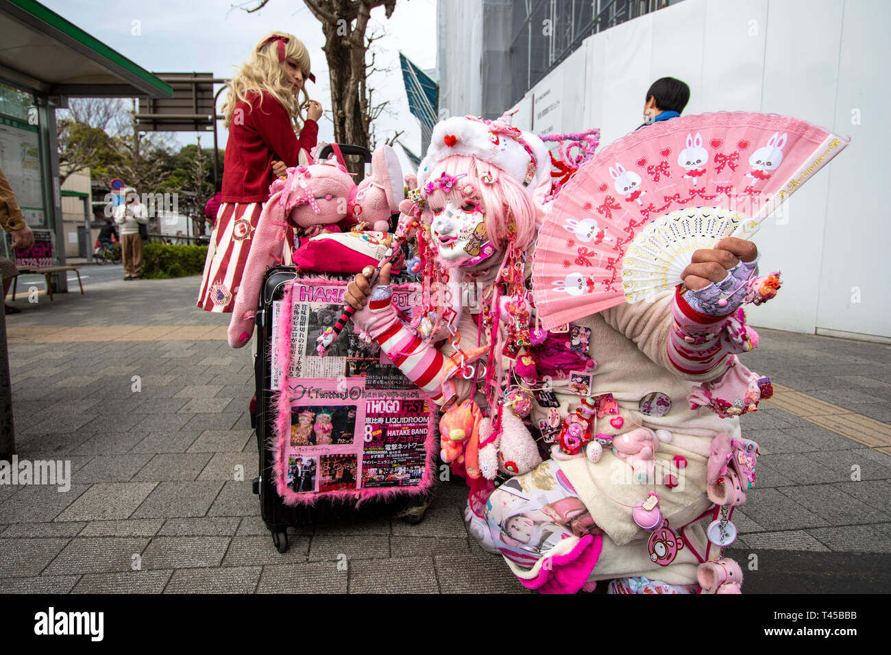 Tokyo, Harajuku è il gioco cos il centro di Tokyo con vari giovani mode in evidenza. Questo uomo, noto come Kadocchi, è considerato come egli unoffical icona di Harajuku. Uomo vestito da clown in rosa e bianco vestito mantenendo la ventola, in posa per il visualizzatore. Contatto visivo. Foto Stock