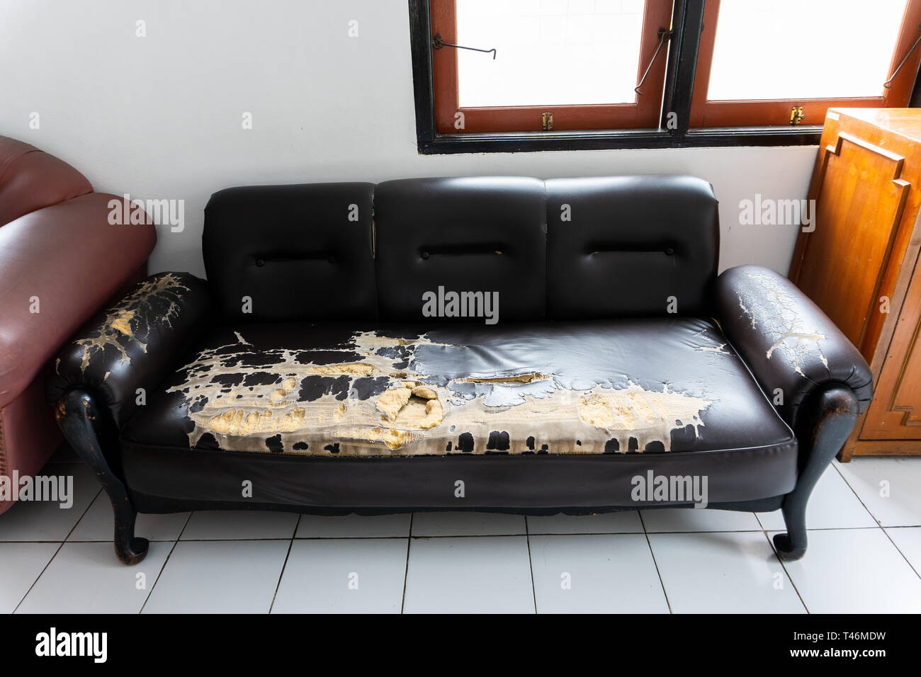 Rotto e vecchio divano marrone sedie in una piccola stanza con pavimento bianco Foto Stock