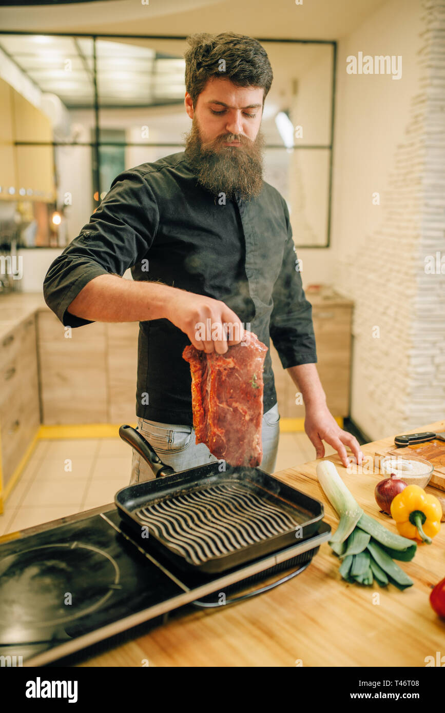 Barbuto chef cucinare la carne in una padella in cucina Foto Stock