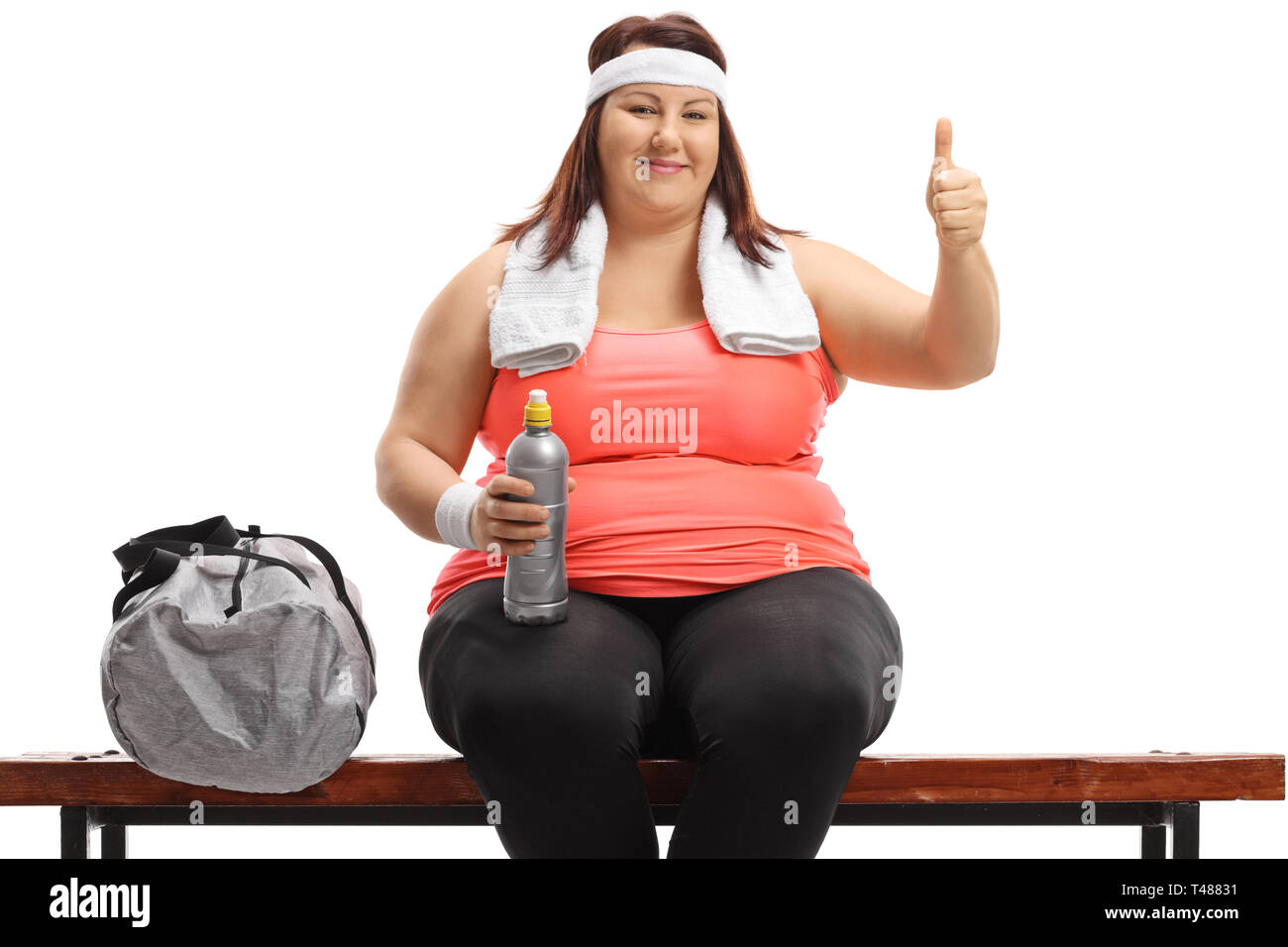 Taglie donna seduta su una panchina di legno accanto a una borsa sportiva rendendo un pollice in alto segno isolato su sfondo bianco Foto Stock