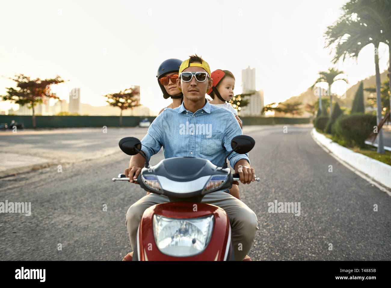 I genitori con il loro bambino in sella motocicletta sulla soleggiata città street Foto Stock