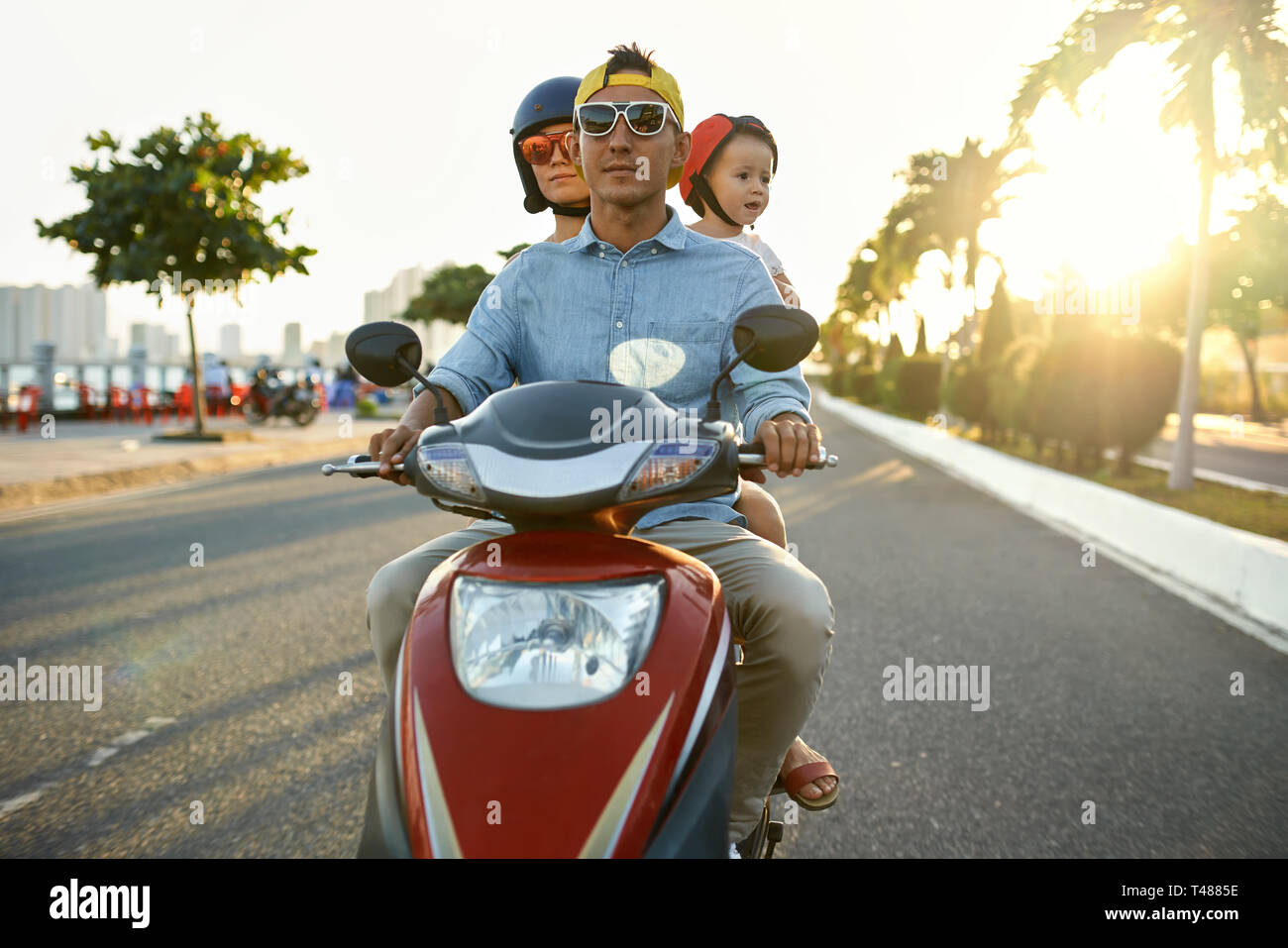 I genitori con il loro bambino in sella motocicletta sulla soleggiata città street Foto Stock