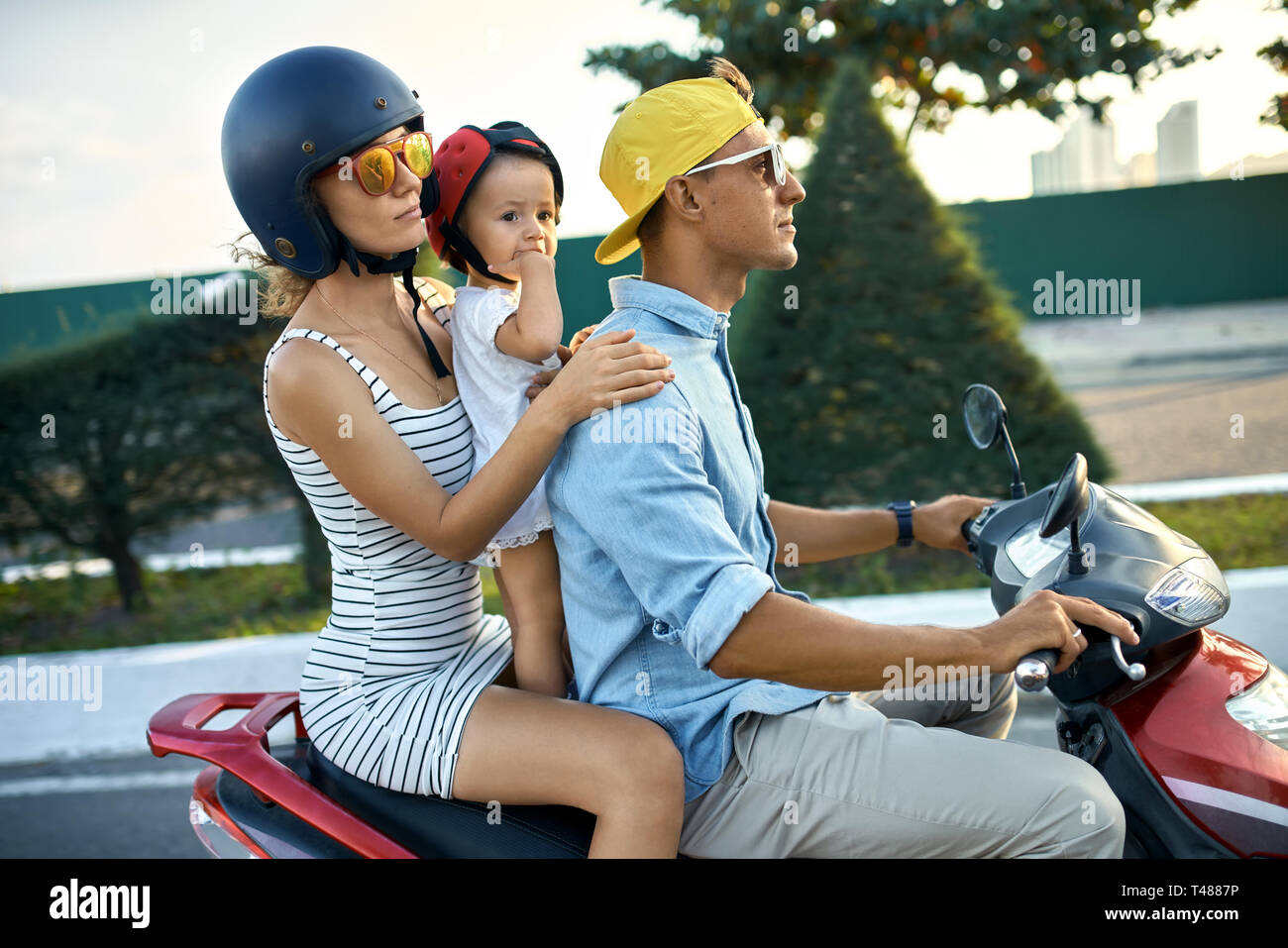 I genitori con i loro bambini in sella motocicletta sulla soleggiata città street Foto Stock