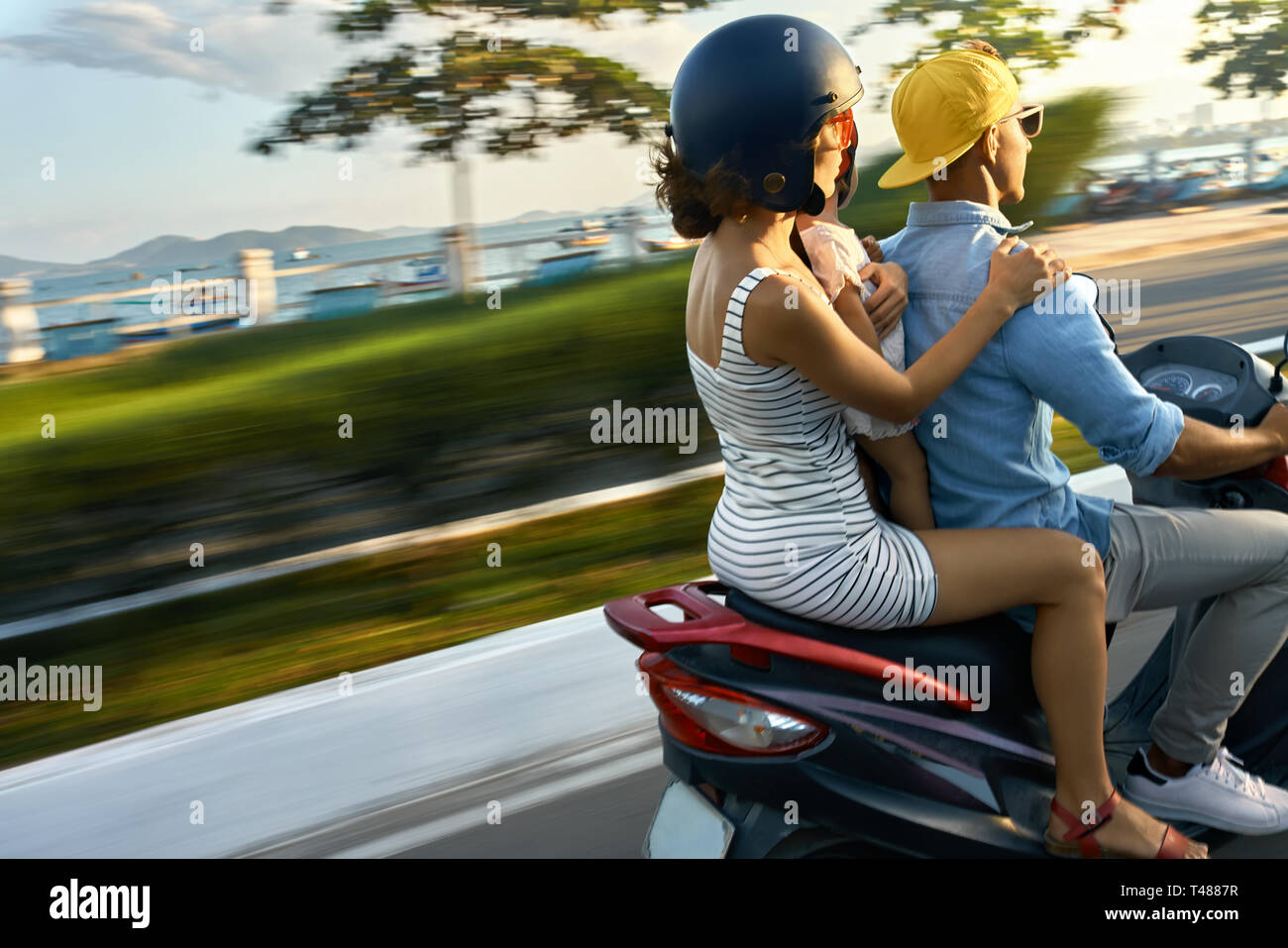 I genitori con i loro bambini in sella motocicletta sulla soleggiata città street Foto Stock