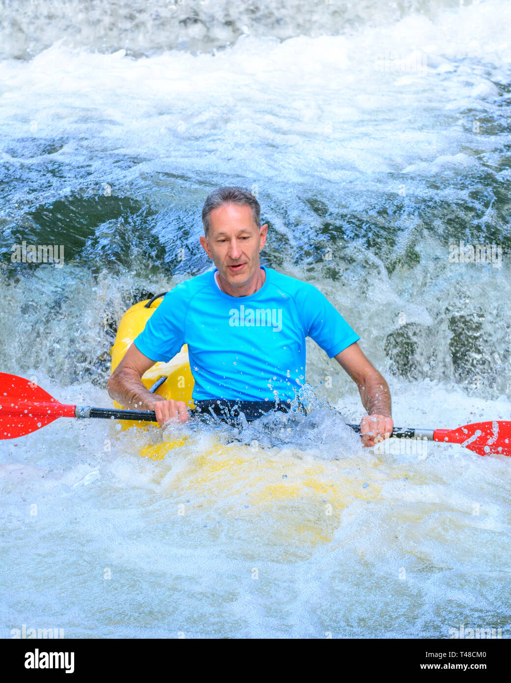 Kayaker paddling in basso uno stramazzo sulle rive di un fiume Foto Stock