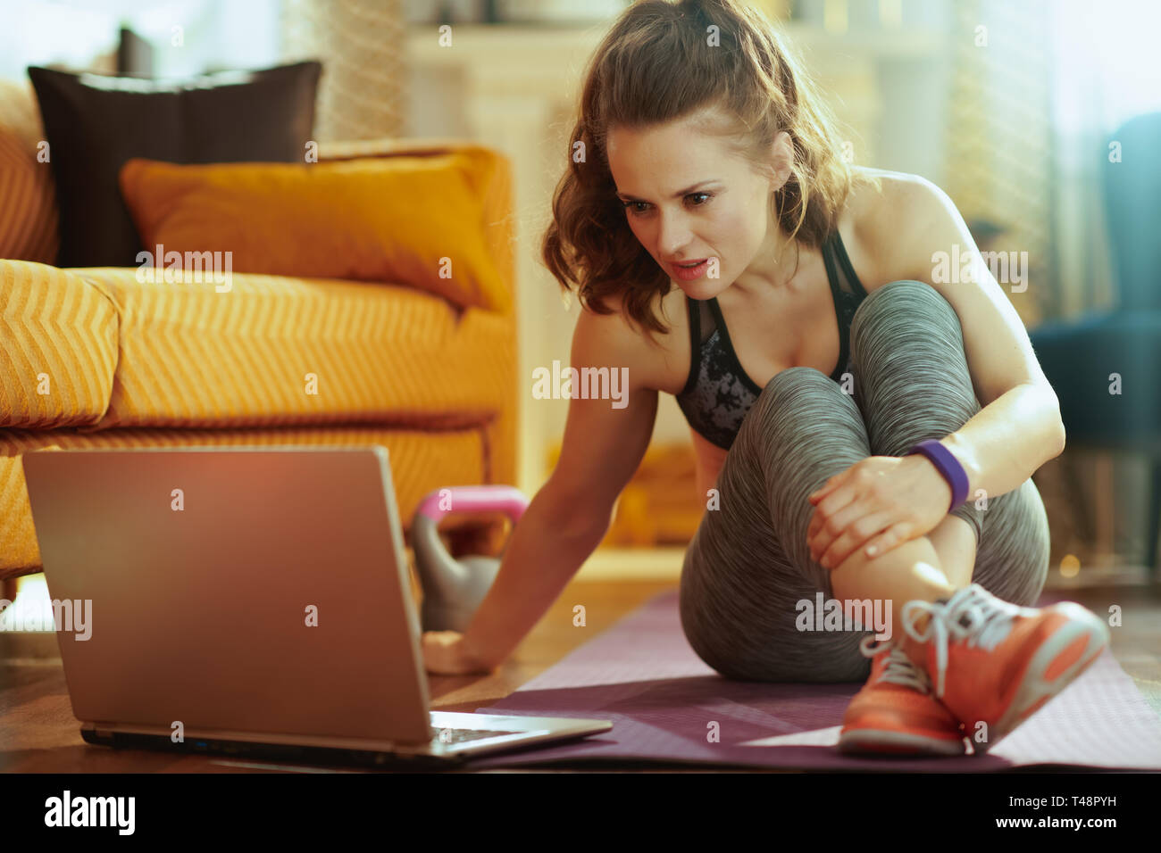 Sport giovane donna in abiti sportivi nel soggiorno moderno utilizzando il notebook per condividere i risultati della sessione in social media. Foto Stock