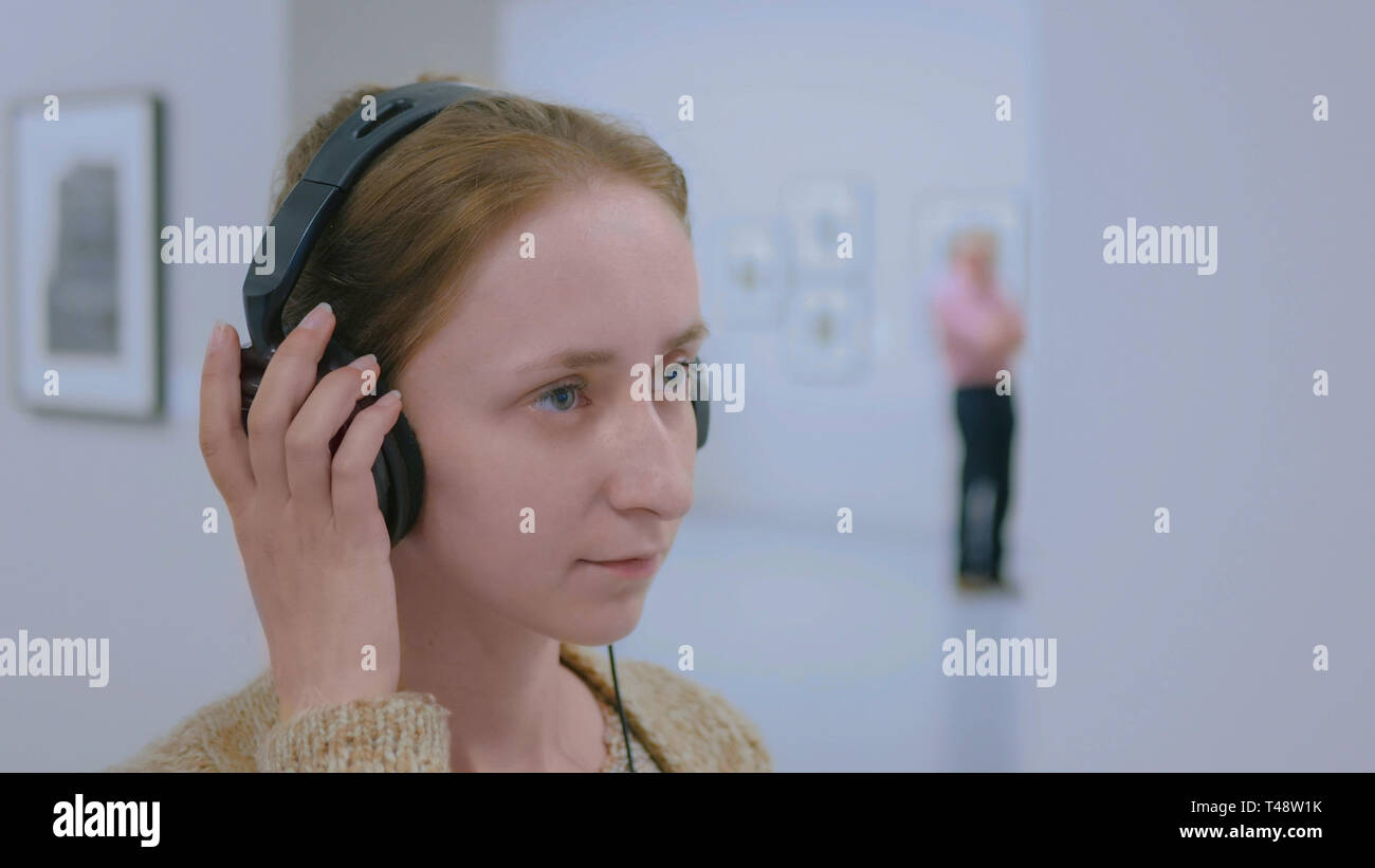 Donna che guarda la esposizione, utilizzando le cuffie e ascolto audio guida Foto Stock