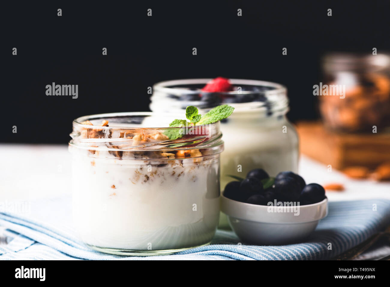Un vasetto di yogurt con cereali e frutti di bosco sulla tavola su sfondo nero con copia spazio per il testo Foto Stock