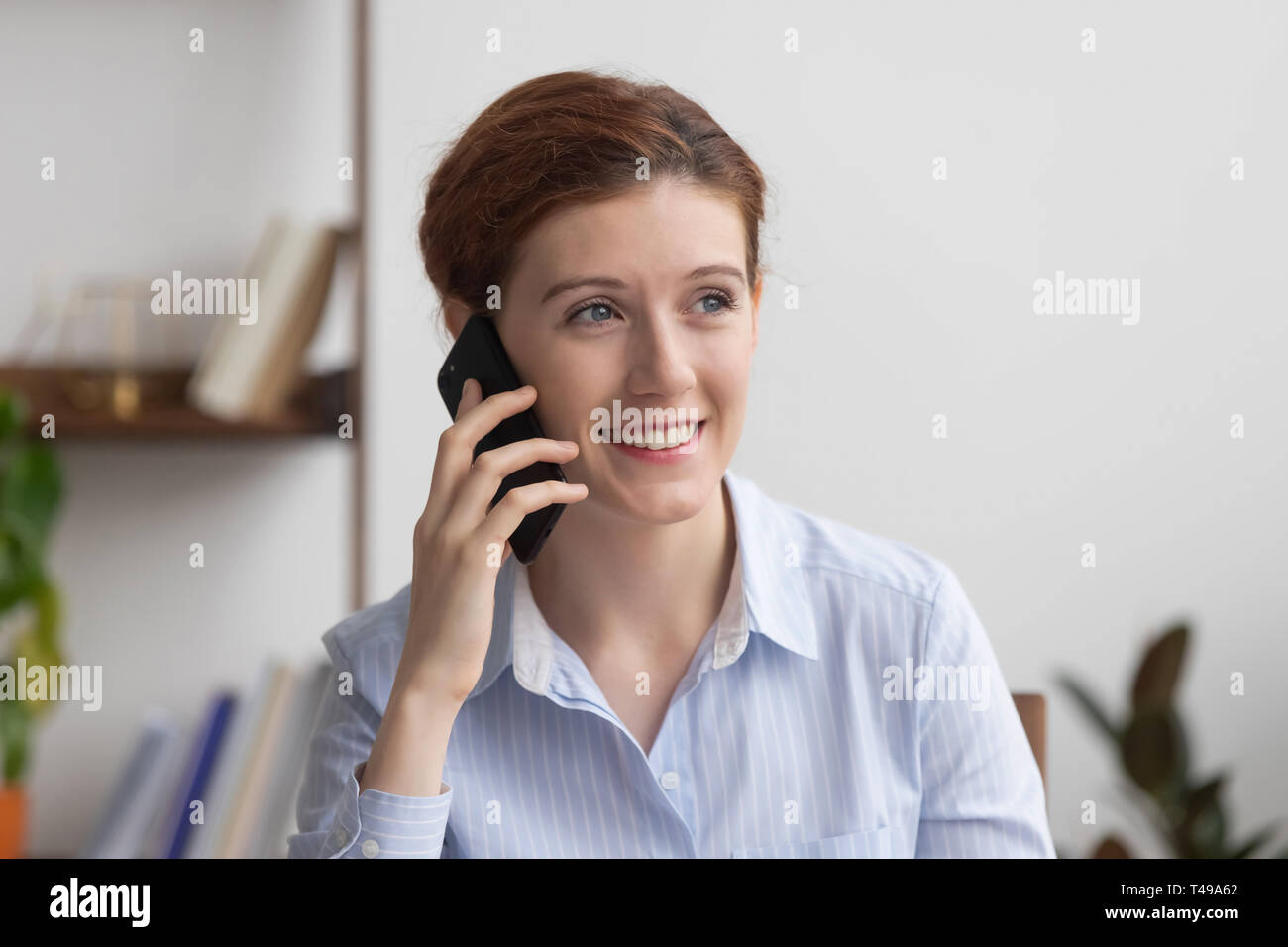 Sorridente imprenditrice millenario parlando al telefono in ufficio durante il lavoro Foto Stock