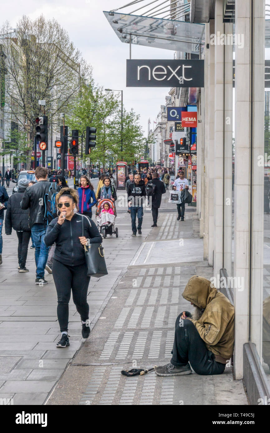 La gente che passa un uomo a mendicare per Oxford Street nel West End di Londra. Foto Stock