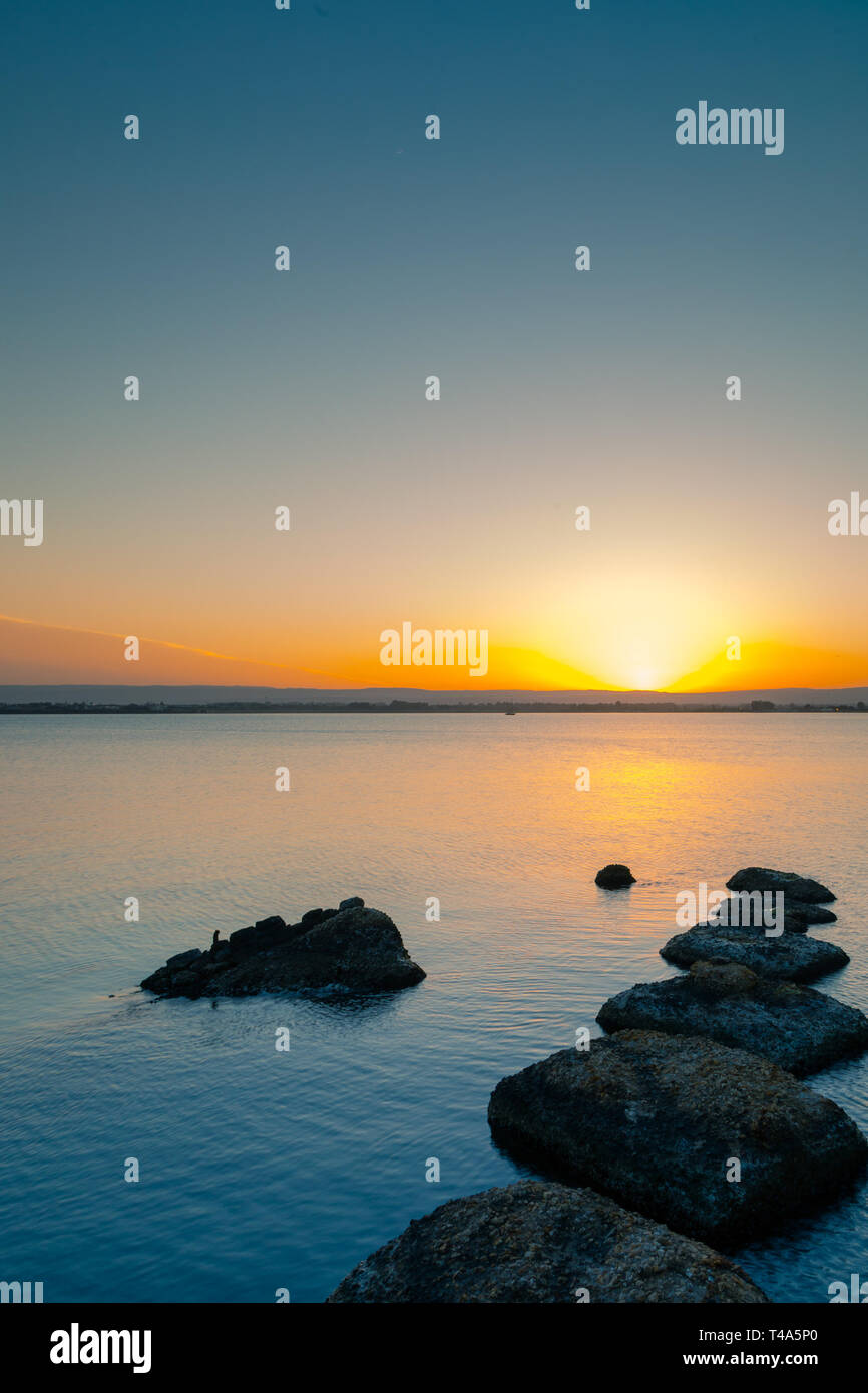 Tramonto sulla calma acqua, rocce in primo piano Foto Stock
