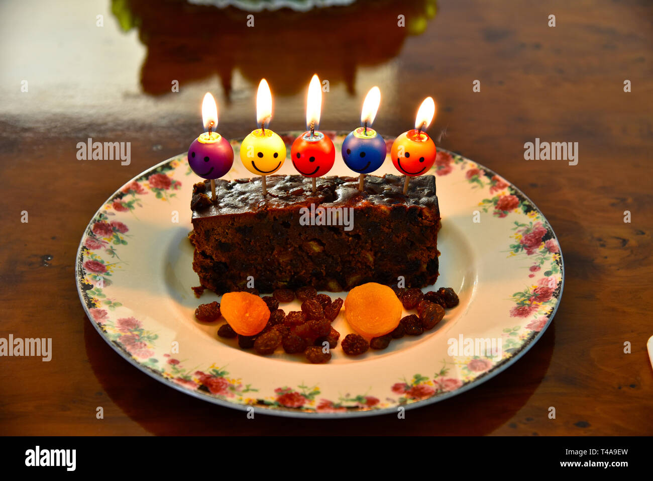 Torta di compleanno con il volto sorridente di candele accese sulla cima di una tavola di legno Foto Stock