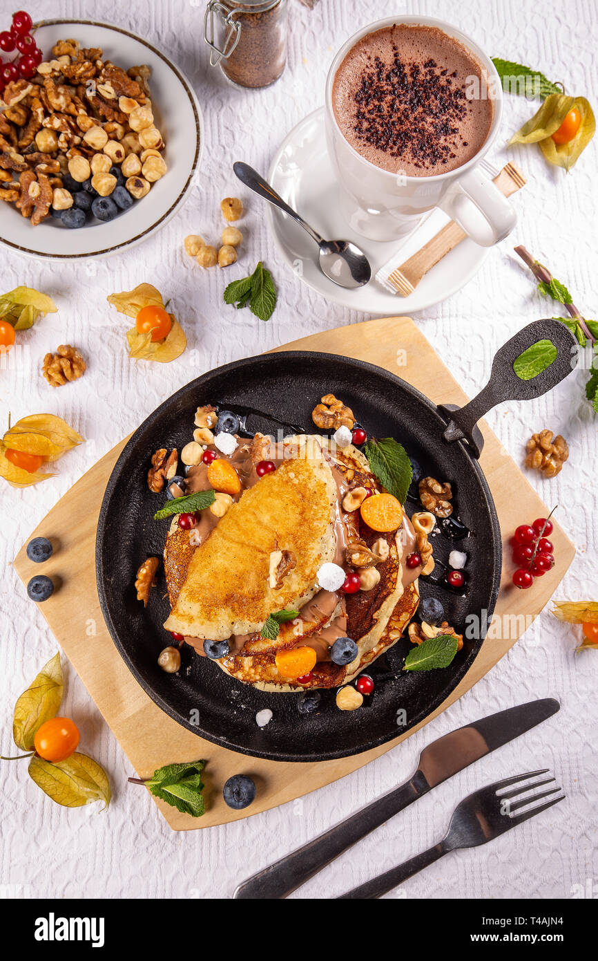 Lay piatto di frittelle con frutti di bosco, dadi e salsa al cioccolato servito per la prima colazione Foto Stock