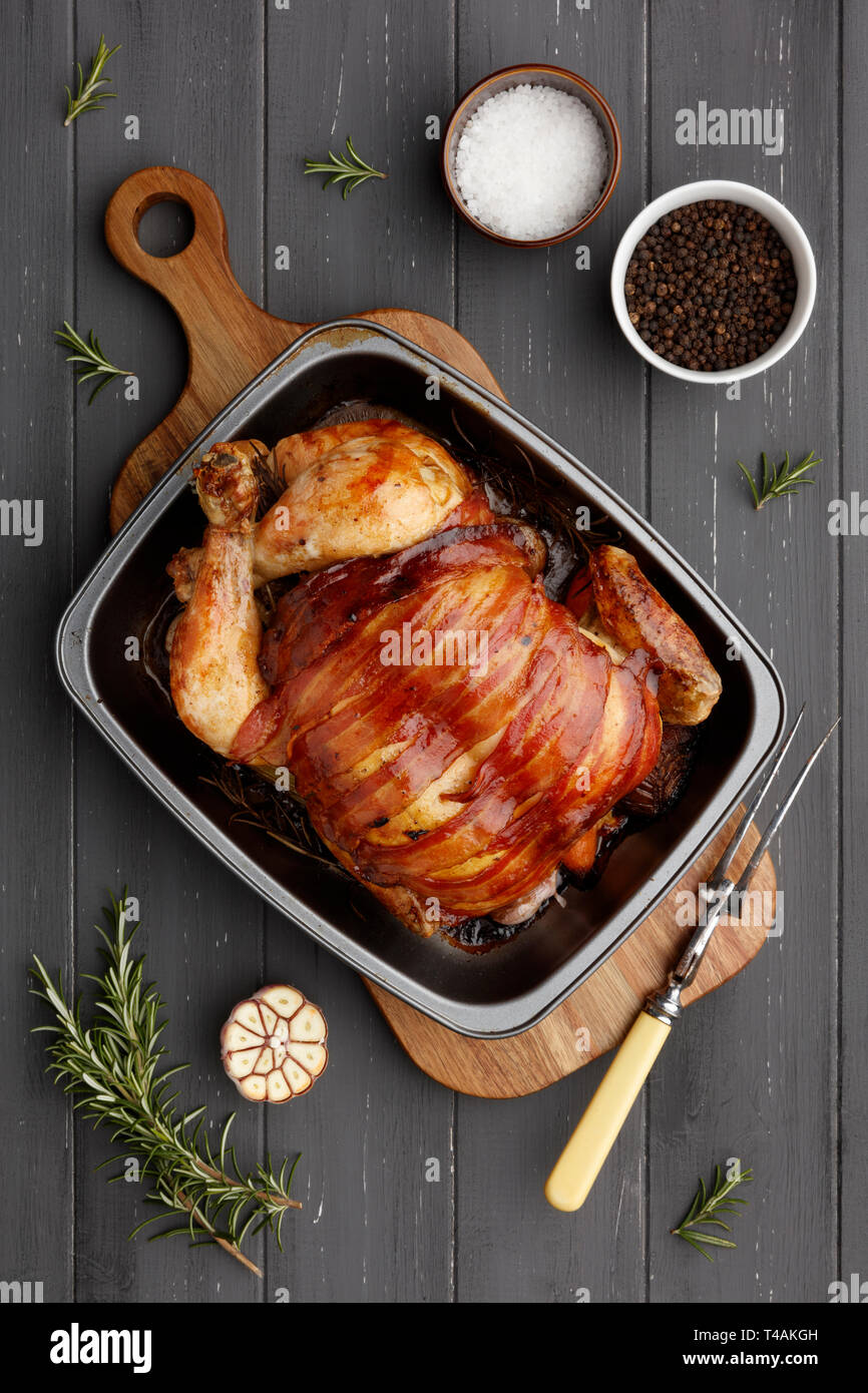 Pollo arrosto in un stagno rasting con ingredienti e forchettone su un grigio scuro dello sfondo in legno Foto Stock
