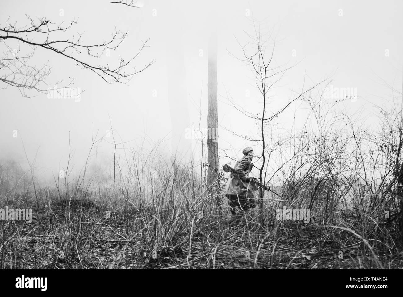 Ri-enactor vestito di sovrarivestimento come guerra mondiale II Soviet russo Rosso soldato dell'esercito in esecuzione in fumo antinebbia con la mitragliatrice nel Bosco Nebbioso di massa. Foto in Foto Stock