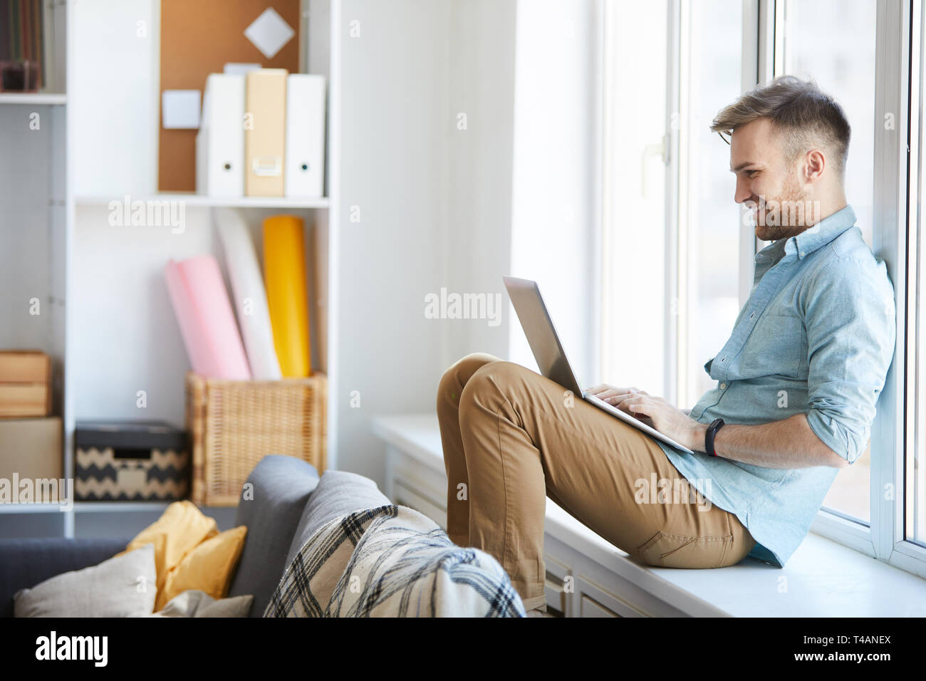 Giovane uomo utilizzando Laptop dalla finestra Foto Stock