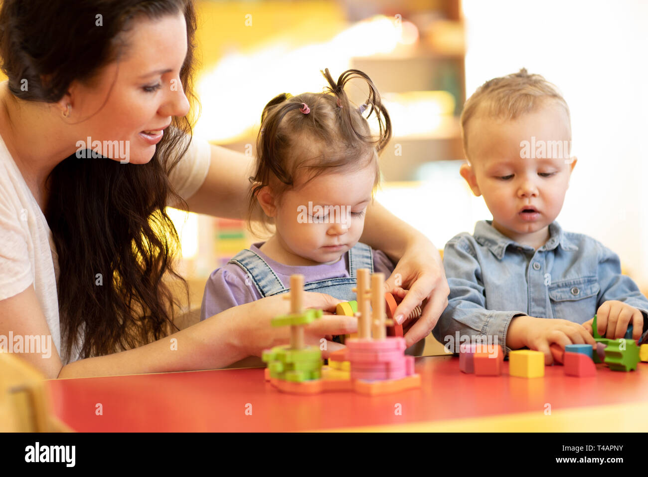 I bambini con insegnante giocare con forme e colorati puzzle in legno in un aula montessori Foto Stock