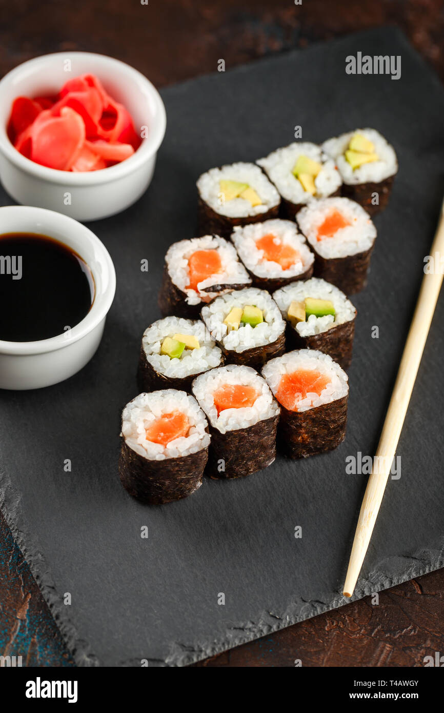 I sushi giapponesi Le bobine servita su pietra ardesia su sfondo scuro. Sushi rotoli maki, zenzero sott'aceto e salsa di soia. Sfondo di sushi. Asian o giapponese fo Foto Stock
